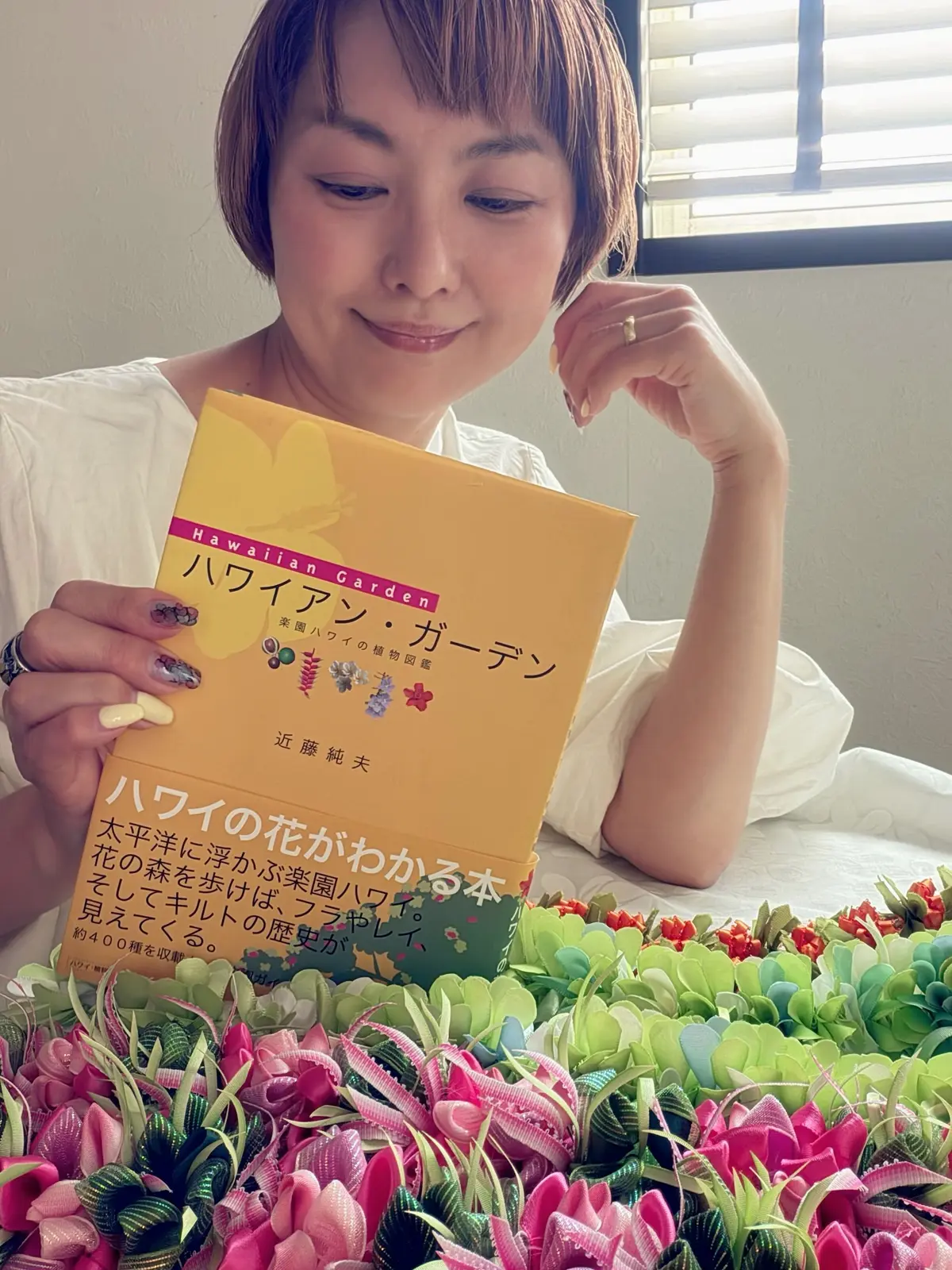 ハワイアンガーデンの本を持つ女性、周囲に色とりどりの人工花が広がる