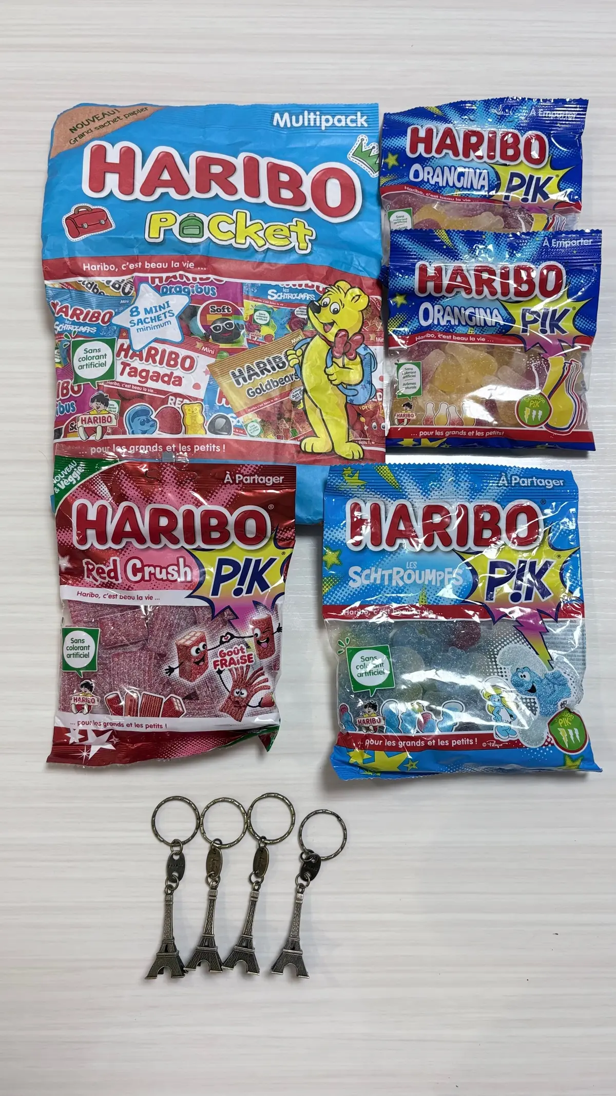 白いテーブルの上に置かれた、ハリー・ポッターとハリボーの商品の写真。左にはハリボーマルチパックの袋が並び、右にはハリボーオレンジナ、レッドクラッシュ、シュトゥルンプスの袋が置かれている。