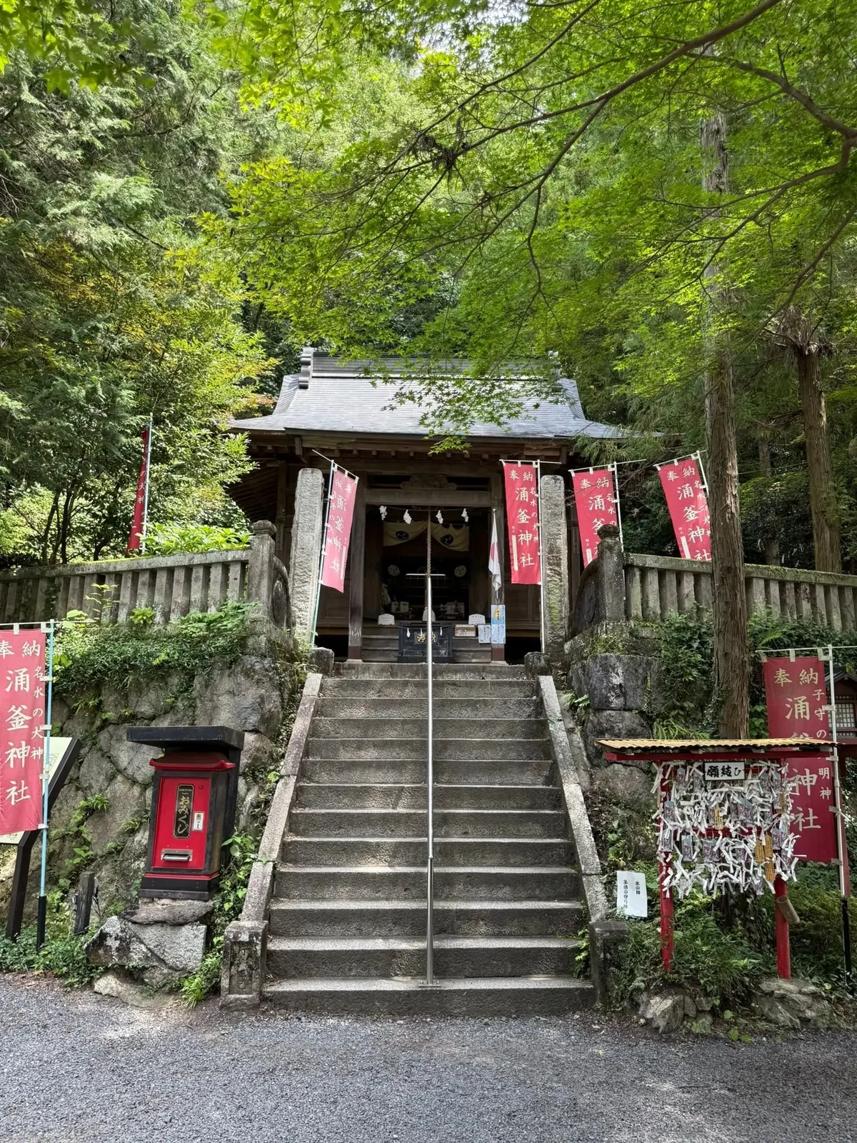 緑豊かな木々に囲まれた、階段の上にある伝統的な日本の神社。朱色の鳥居が並び、建物は木造で屋根は急勾配。石段を上がると神社の入り口があり、静寂な雰囲気が伝わる。