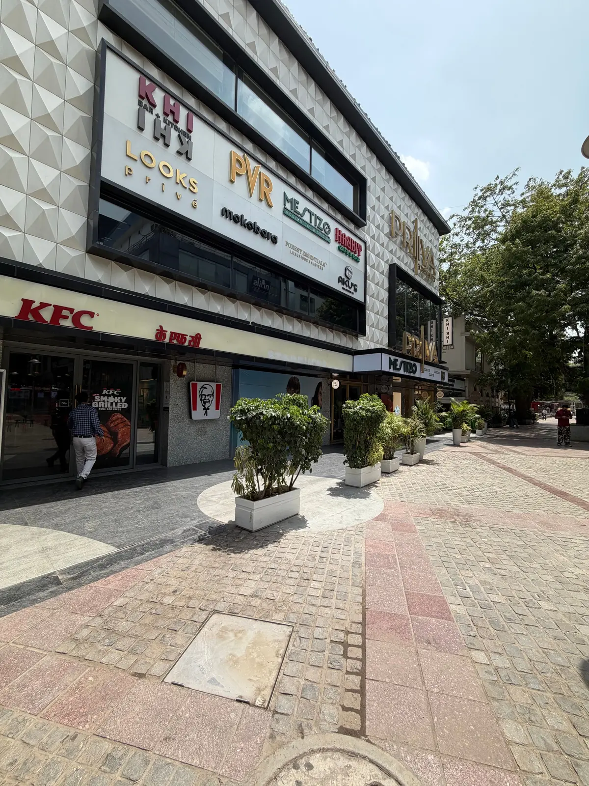 KFCの店舗入り口と周辺に配置された緑の植物、通路はレンガ調の舗装が施されている