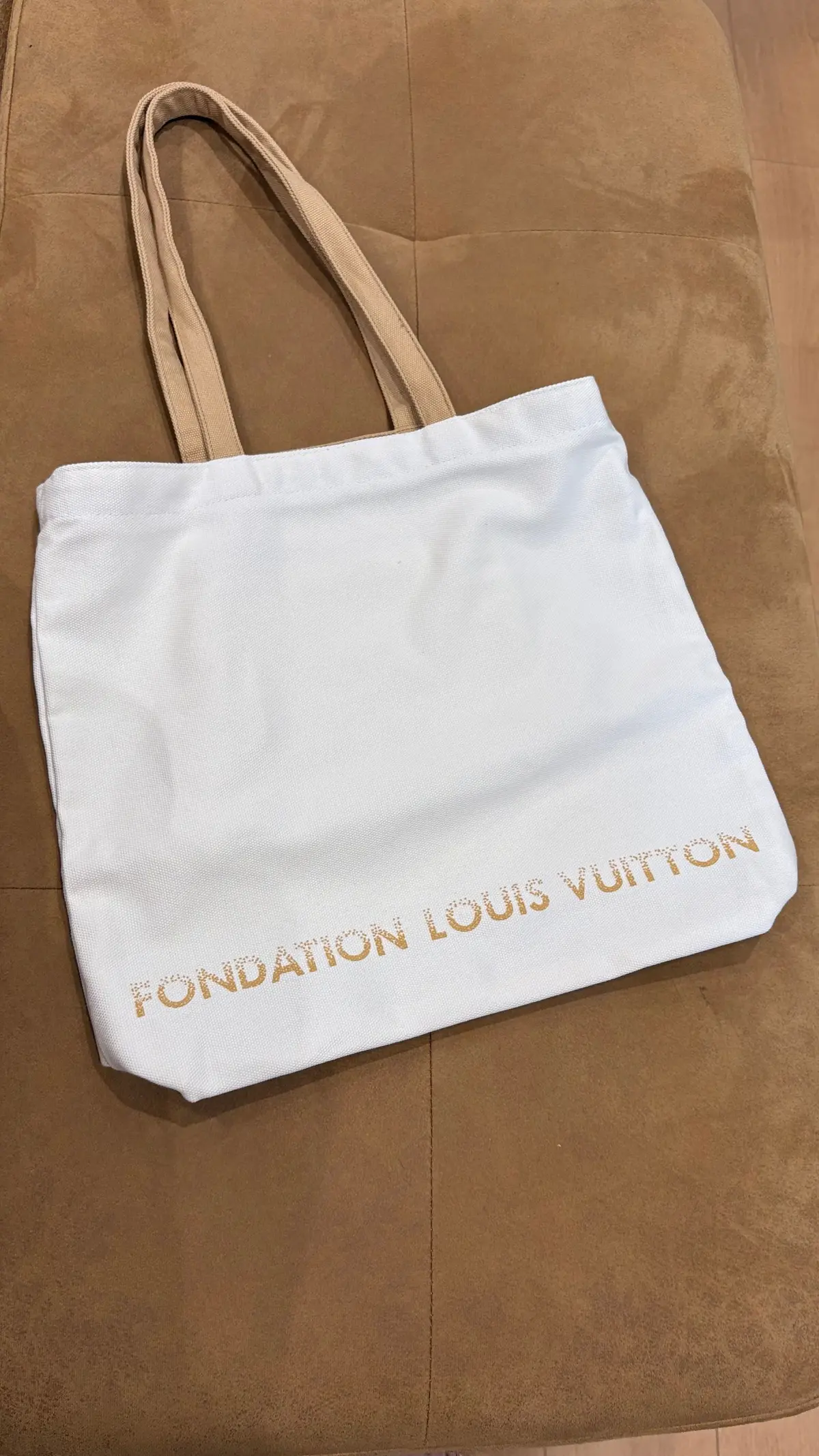 白いキャンバス地のトートバッグ。ベージュ色の持ち手が付いており、「FONDATION LOUIS VUITTON」のロゴが白文字でプリントされている。