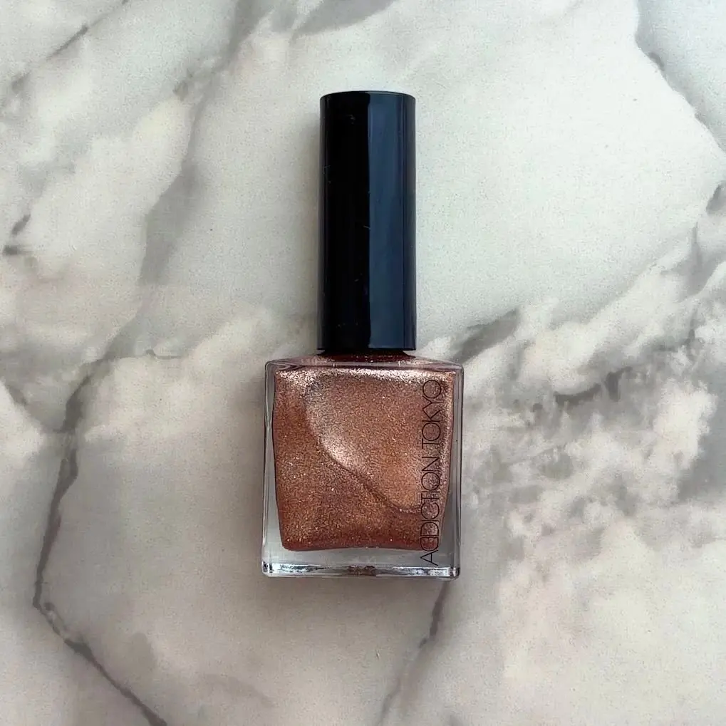 アディクションのTHE NAIL POLISH + 131sp コスタブロンズネイル、シルバーラメ輝くブロンズカラー、大理石のボードの上に置かれています