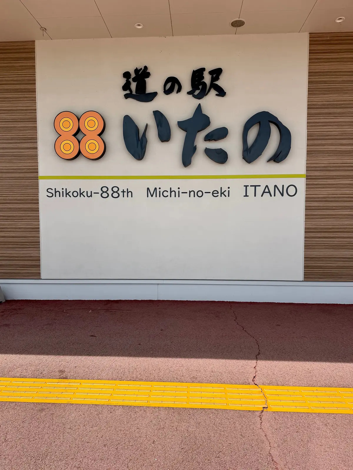 シコク88番目の道の駅「いたの」の案内板。茶色とベージュの建物に設置され、駅名と「Shikoku-88th Michi-no-eki ITANO」の文字が記載されている。