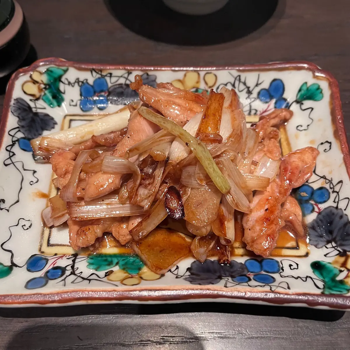 和風の模様が描かれた長方形の皿に盛り付けられた、豚肉と大根の煮物。照り気のある薄切り肉と、白く太めの大根が混ざり合っている。