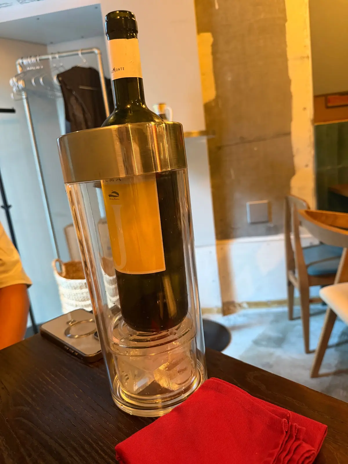 ボトル入りワインが氷入りの透明な容器に入れられ、テーブルに置かれている。赤い布が横に置かれている。