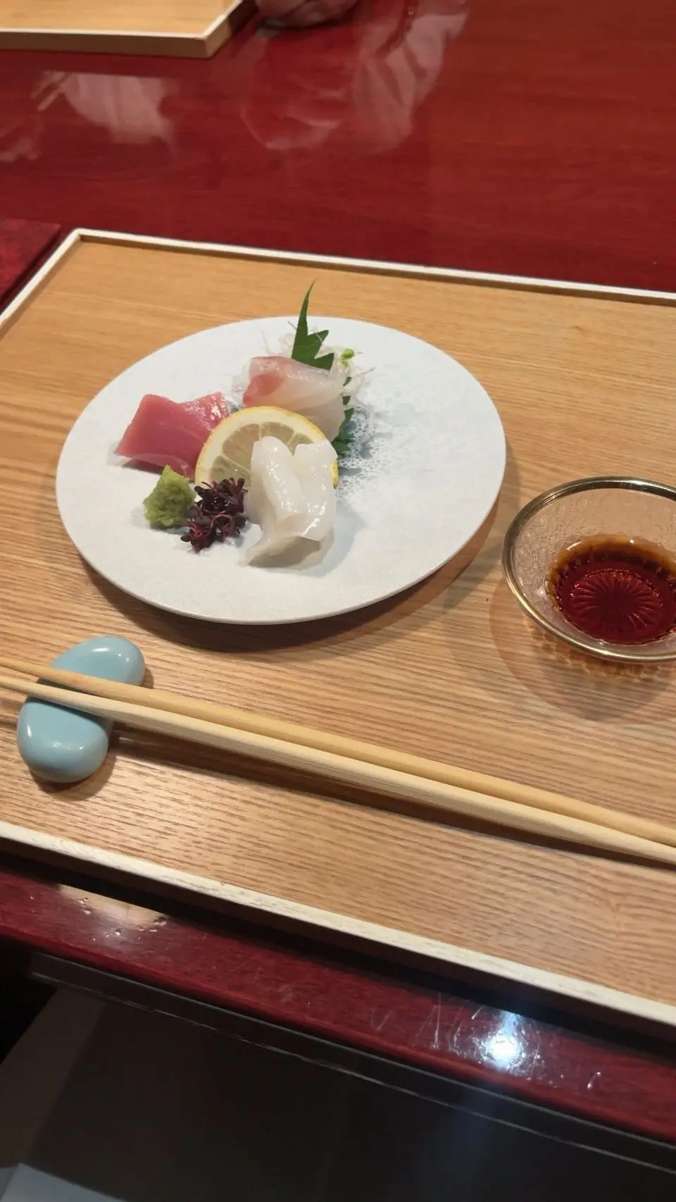 白いプレートにサーモン、レモン、わさび、ワサビ、海老、ウニが配置された刺身料理。木製のテーブルに青い石と箸が置かれている。
