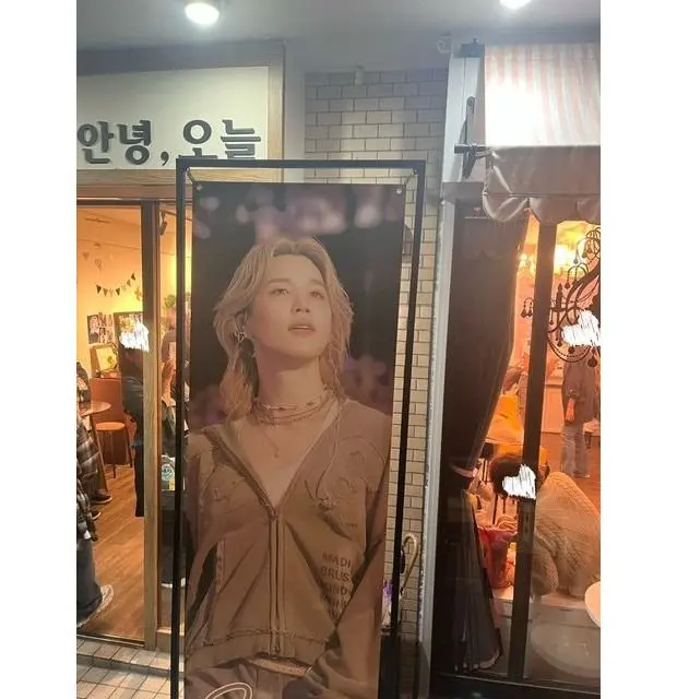 BTSのジミン（Park Jimin）の大型ポスターが店の入り口に立てかけられている。背景は白レンガ調で、店名がハングル文字で表示されている。