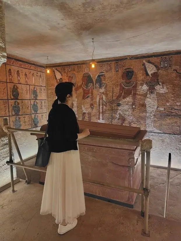 古代エジプトの壁画と石棺が展示された室内。女性が壁画を眺めている。壁画には人物が描かれ、石棺はガラスケース内に設置されている。