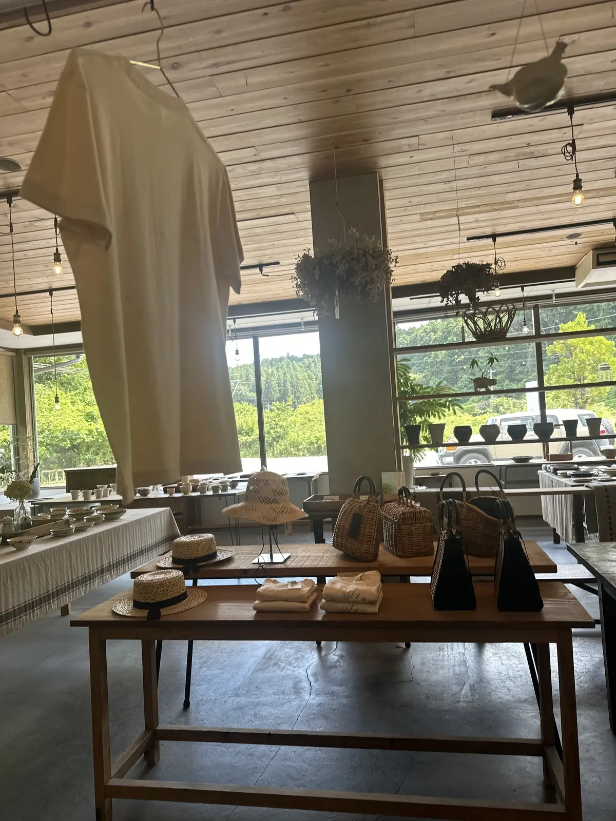 木製の天井と大きな窓から自然光が入る店内には、帽子やカゴバッグ、陶器などが展示された木のテーブルが並ぶ