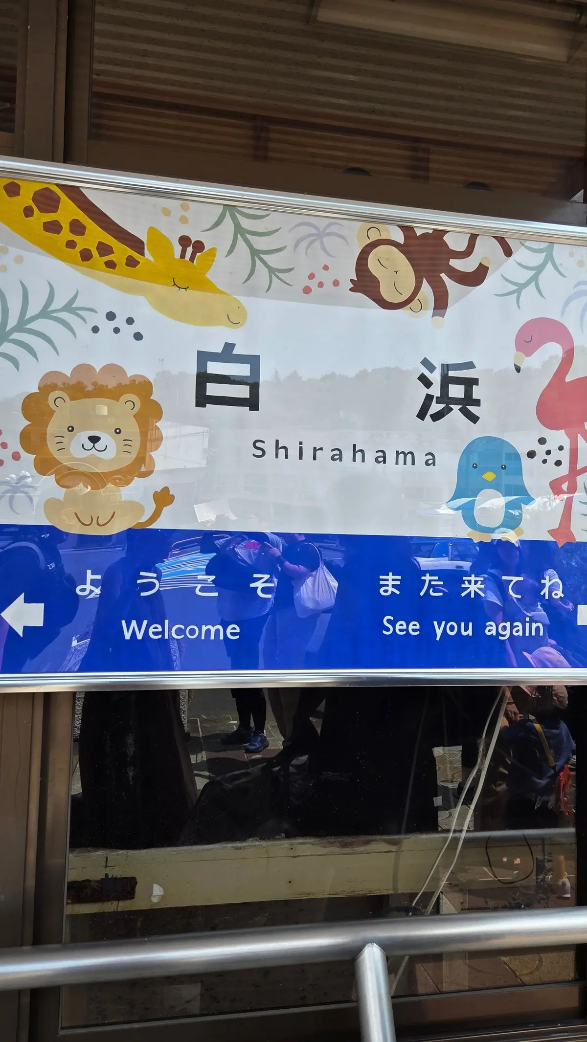 白浜の文字と動物のイラストが描かれた横断幕。左下に「ようこそ Welcome」、右下に「また来てね See you again」の文字。背景に青色のカーテンが見える。