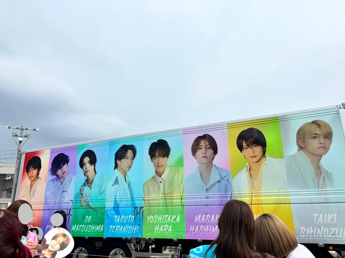 横断幕に、男性アイドルグループ「timelesz」のメンバー8人の写真が並んでいる。各メンバーの背景色は、左から青、水色、白、黄色、ピンク、紫、緑、オレンジ。メンバー名は、各写真の下に記載されている。