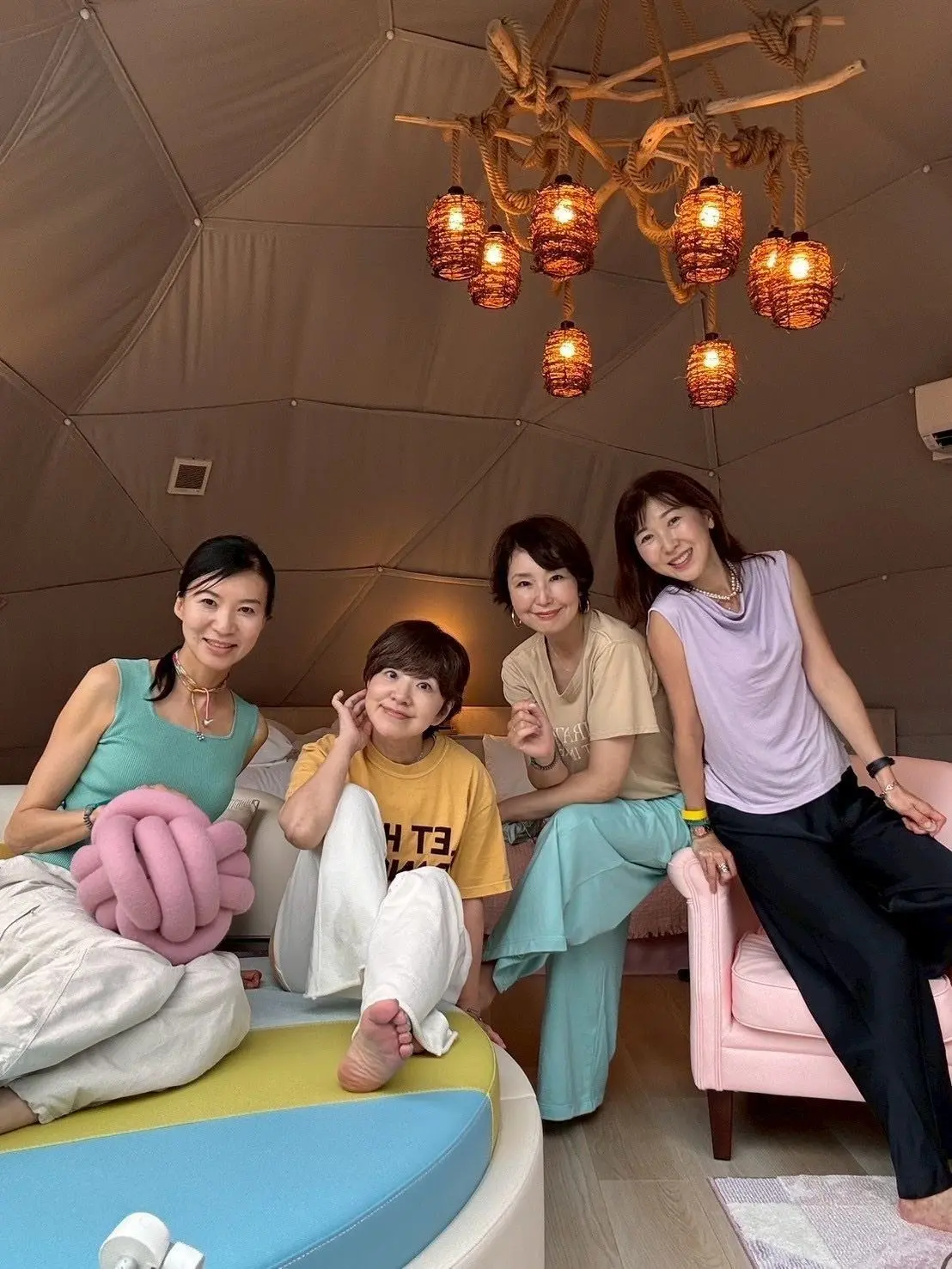 テント内にて、4人の女性がリラックスした姿勢で座り、温かみのあるランプが天井から吊るされています。