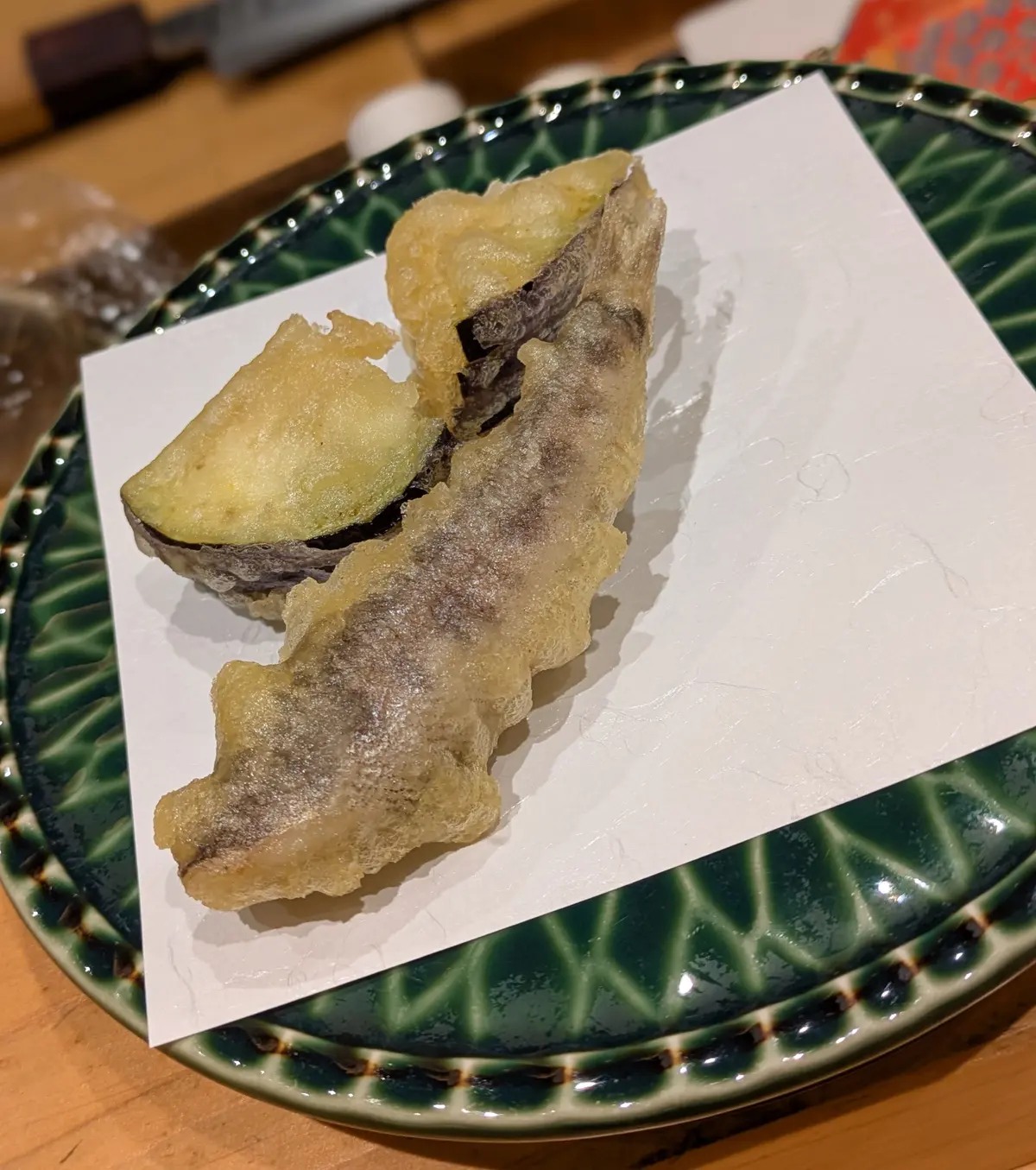 緑の食器に、黄金色の衣がかけられた魚の切り身が2切れ並んでいる。