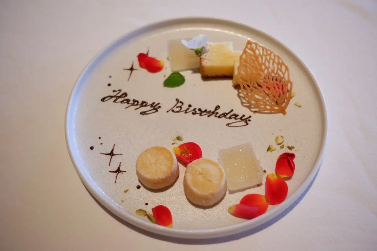 「Happy Birthday 」の文字と花の装飾が施されている。背景には花の生け花とバーカウンターが見える。