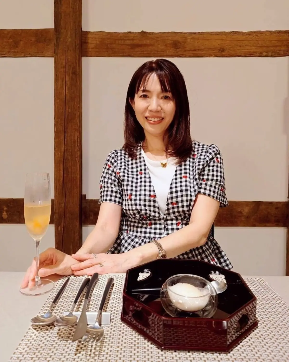 女性はZARAの黒と白のチェック柄のトップスを着用し、金色のアクセサリーを身につけている。背景には木製の柱が見える。佐原商家町ホテルNIPPONIAのルアン