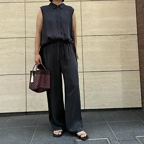 黒色のスリーブレスシャツとワイドパンツのセットアップ。シャツはボタンダウンで裾がアシンメトリー。パンツはウエストにドローストリング入り。両方ともゆったりとしたシルエット。