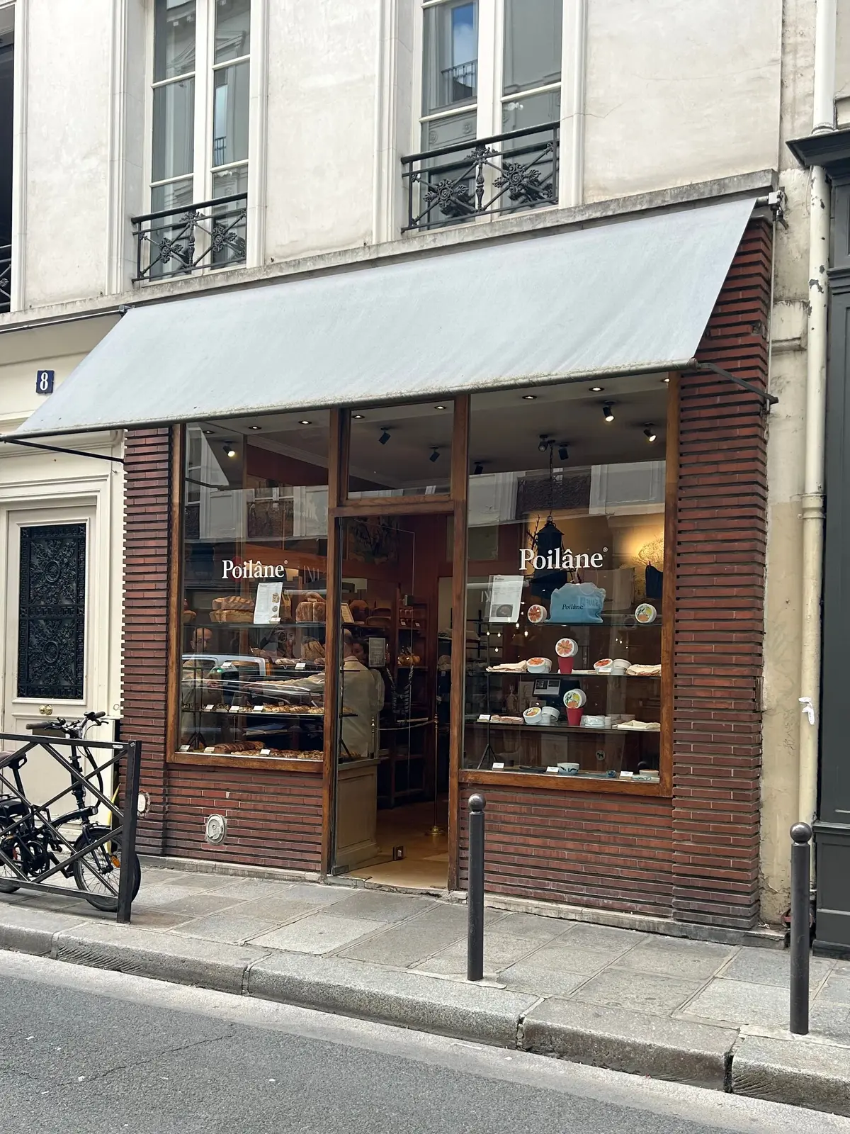 「ポワラーヌ」パン屋の外観。木製の窓枠とガラスのショーケースにパンのディスプレイがあり、店内には明るい照明が設置されている。店前の自転車が停められている。