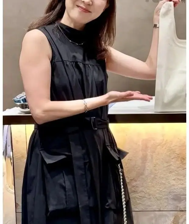 黒いワンピースを着た女性が、右手で白いベビーカーを提示している。左手は軽く開いており、背景にはテーブルと小物が見える。