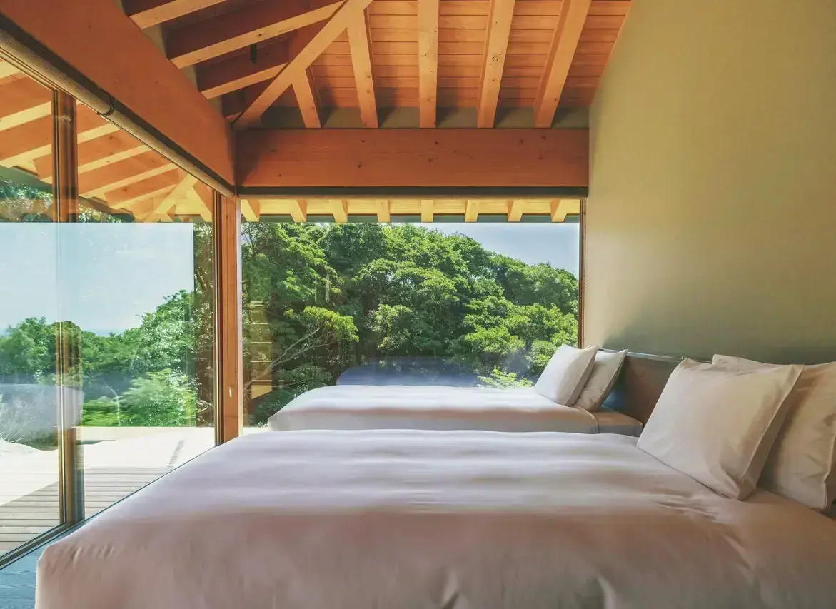 ツインベッドが備わる寝室は、2面がガラス張りで森や庭を眺められる