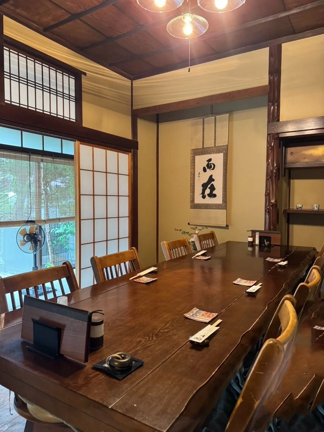 5人の女性が木製テーブルに座り、料理と飲み物を楽しむ。各人の前にはカラフルな料理が並び、ビールやワインのグラスも置かれている。背景には和風の絵画と棚があり、温かみのある雰囲気。