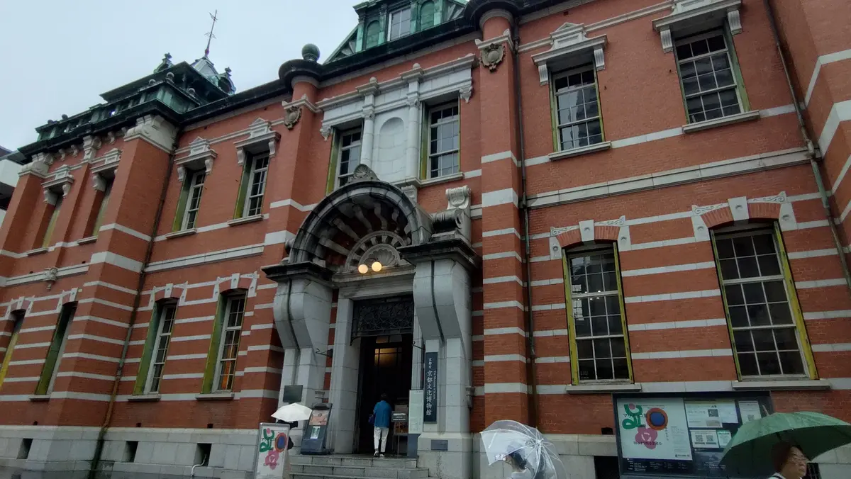 赤レンガ造りの歴史的な建物。中央にはアーチ型の入り口があり、左右に窓が並ぶ。屋根は緑色の瓦で覆われ、装飾的な細部が見られる。