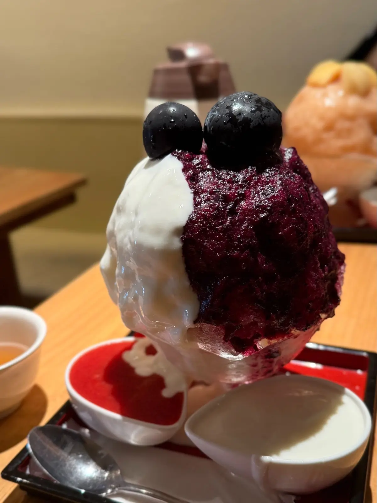 紫と白の雪花氷。丸いブルーベリーが数個乗せられ、赤いソースと白いクリームが添えられている。