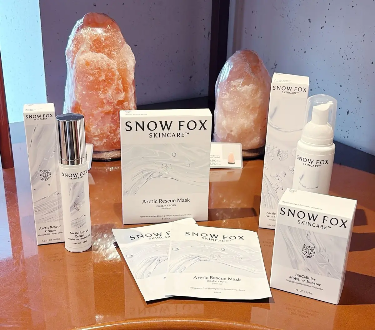 Snow Foxブランドのスキンケア商品が木製テーブルに並ぶ。ボトル、箱、シートマスクがディスプレイされ、製品名と容量が記載されている。