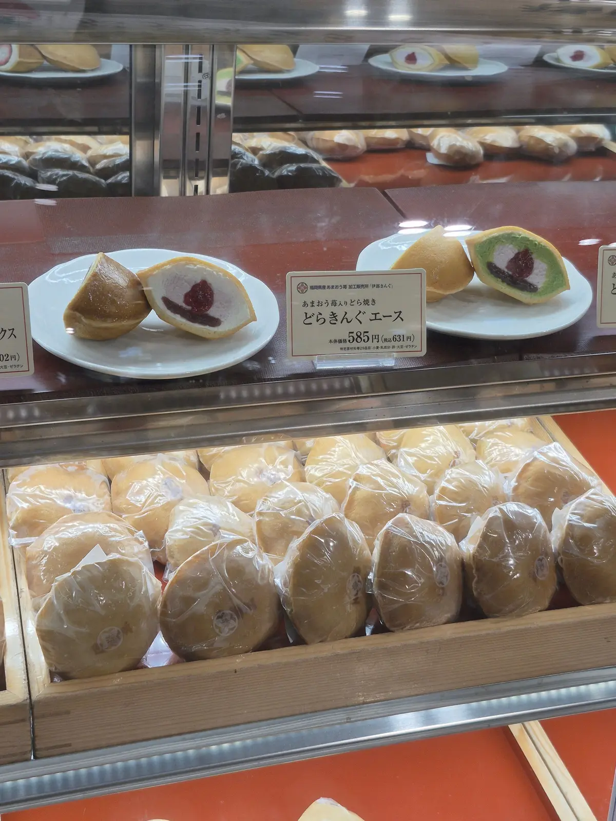 ガラスケースに並んだ様々なお菓子。手前にはパイ生地のようなものが並び、中央には「どらきんぐ エース」と書かれた看板と、パイに赤いソースがかかったものが置かれている。奥には緑色のものが並んでいる。