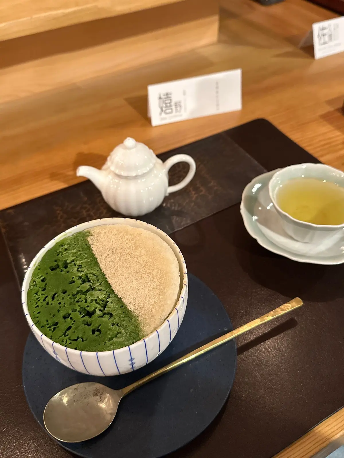 木製のテーブルに置かれた、抹茶と砂糖のセット。青色の器に抹茶と砂糖が別々に入れられ、小さな急須と湯呑みも添えられている。