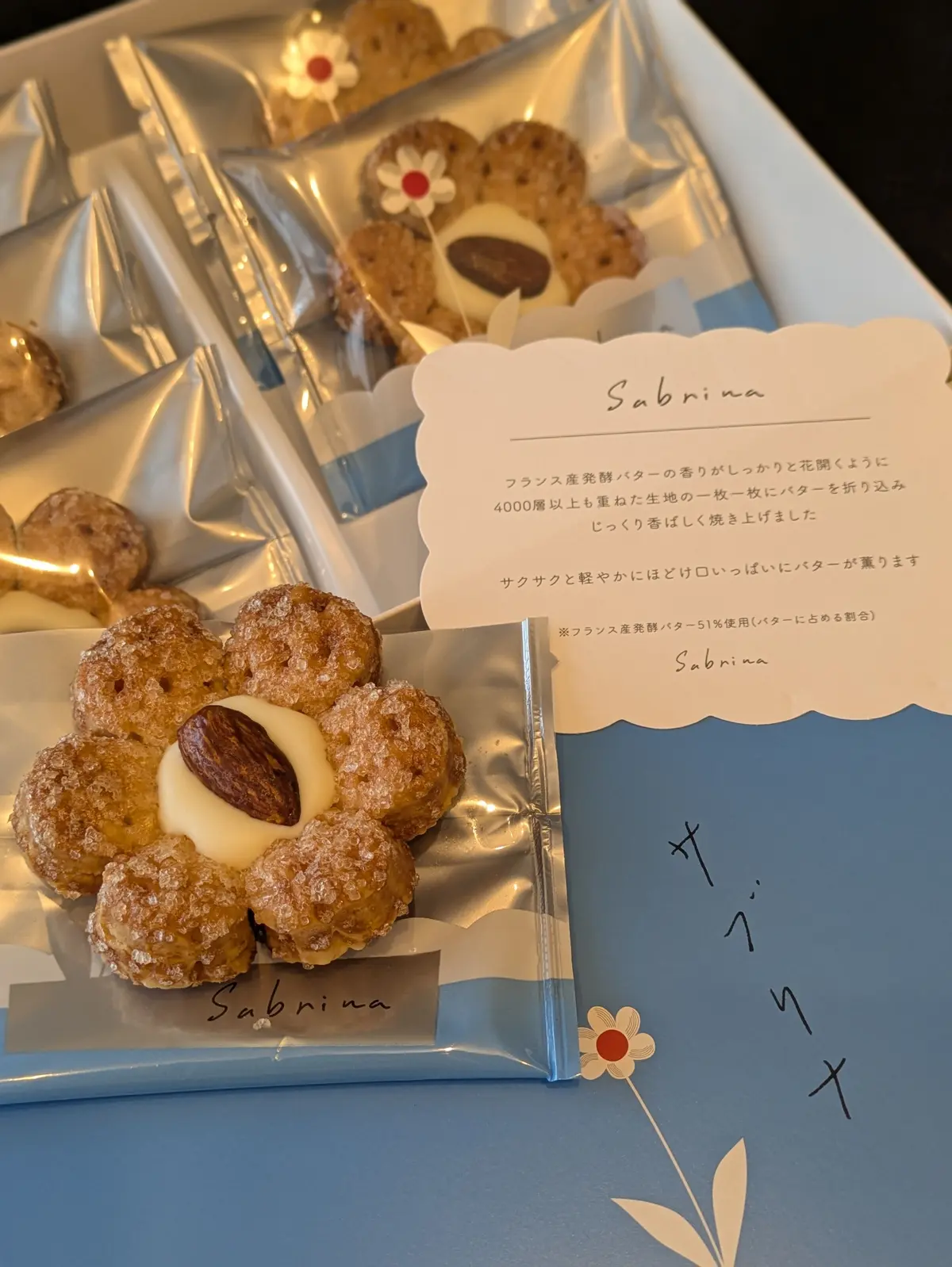 サブリナと書かれた紙に、花の形をしたサクサクしたクッキーと、中央にアーモンドとクリームが入ったデザートが並ぶ