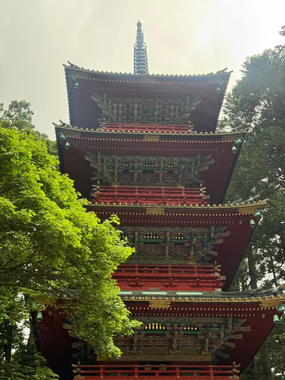 多層の赤い寺院塔、緑の木々の中で装飾が施された詳細な構造と尖った頂部が特徴