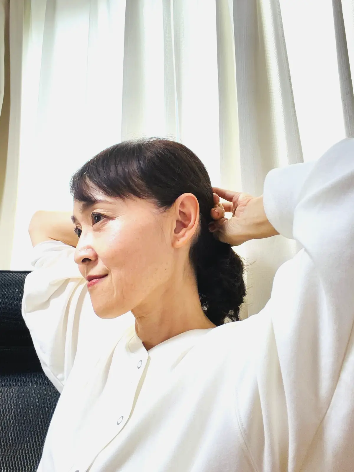 白シャツを着た女性が、首の後ろに手を回し、髪を束ねている。