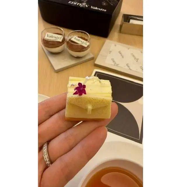 Valextraの高級菓子セット。2つのミニカップケーキと、レモン風味のタルト、茶葉が置かれた白地のテーブル。タルトには紫色の花が飾られている。