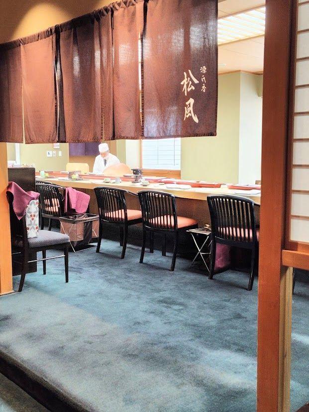 寿司カウンターに椅子が並び、背後には調理員が立つ和食レストランの内装