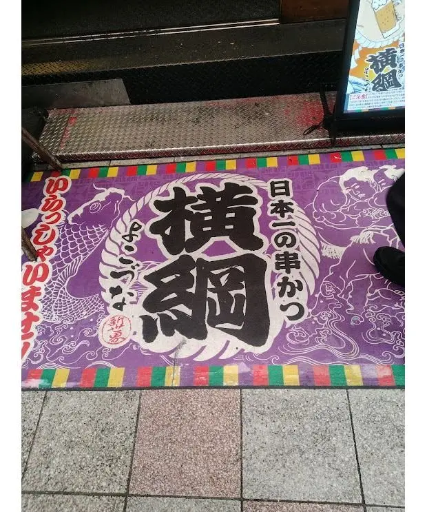 紫色の背景に、大きな「横綱」の文字が描かれたマット。右上に日本の朝食のメニューが立てかけられている。マットの周囲には、波や龍の絵柄が配置されている。