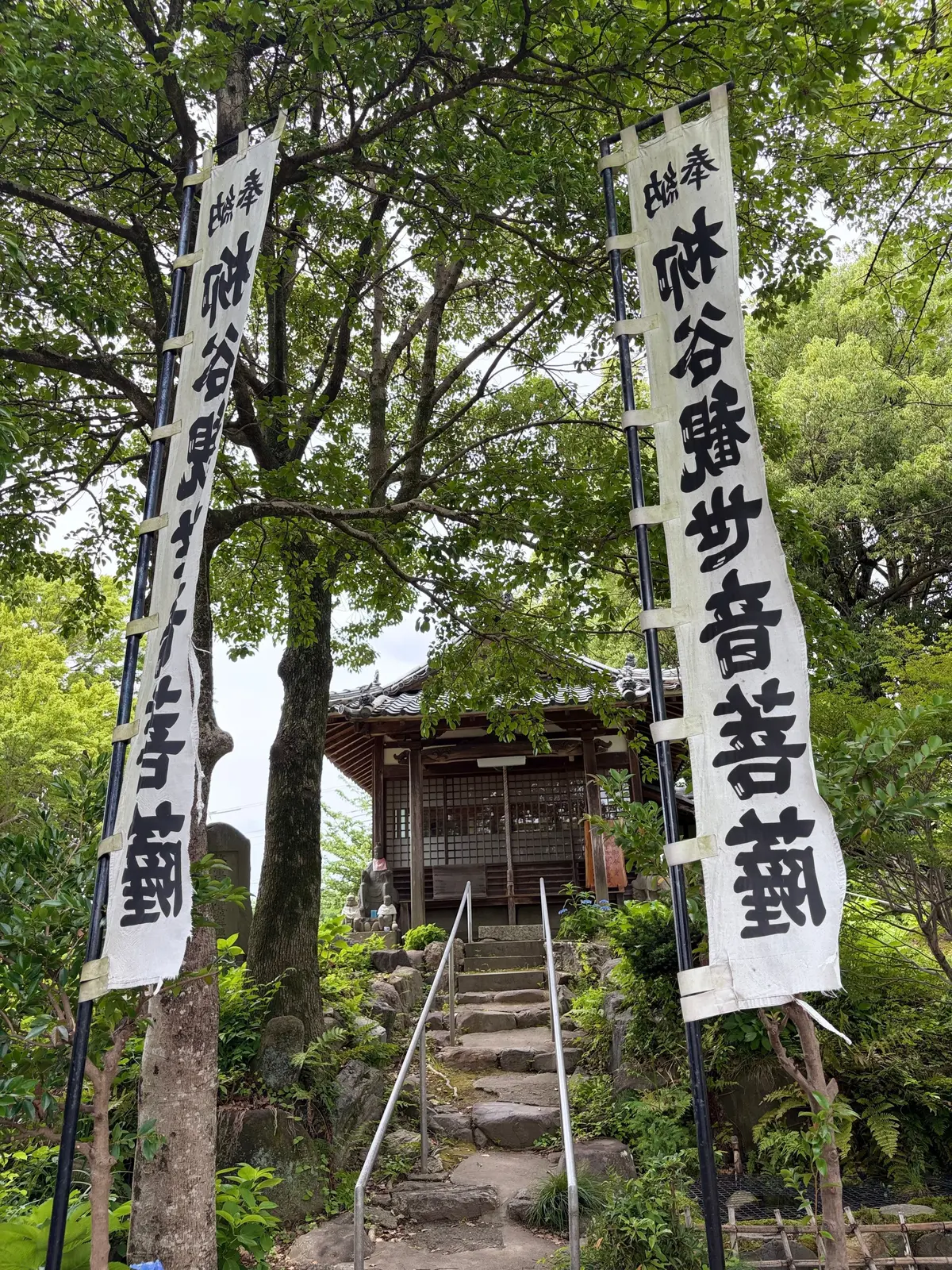 緑豊かな庭園に石段があり、両側に「ご供養」の文字が書かれた白い提灯が立てられている。奥には木造の建物が見える。