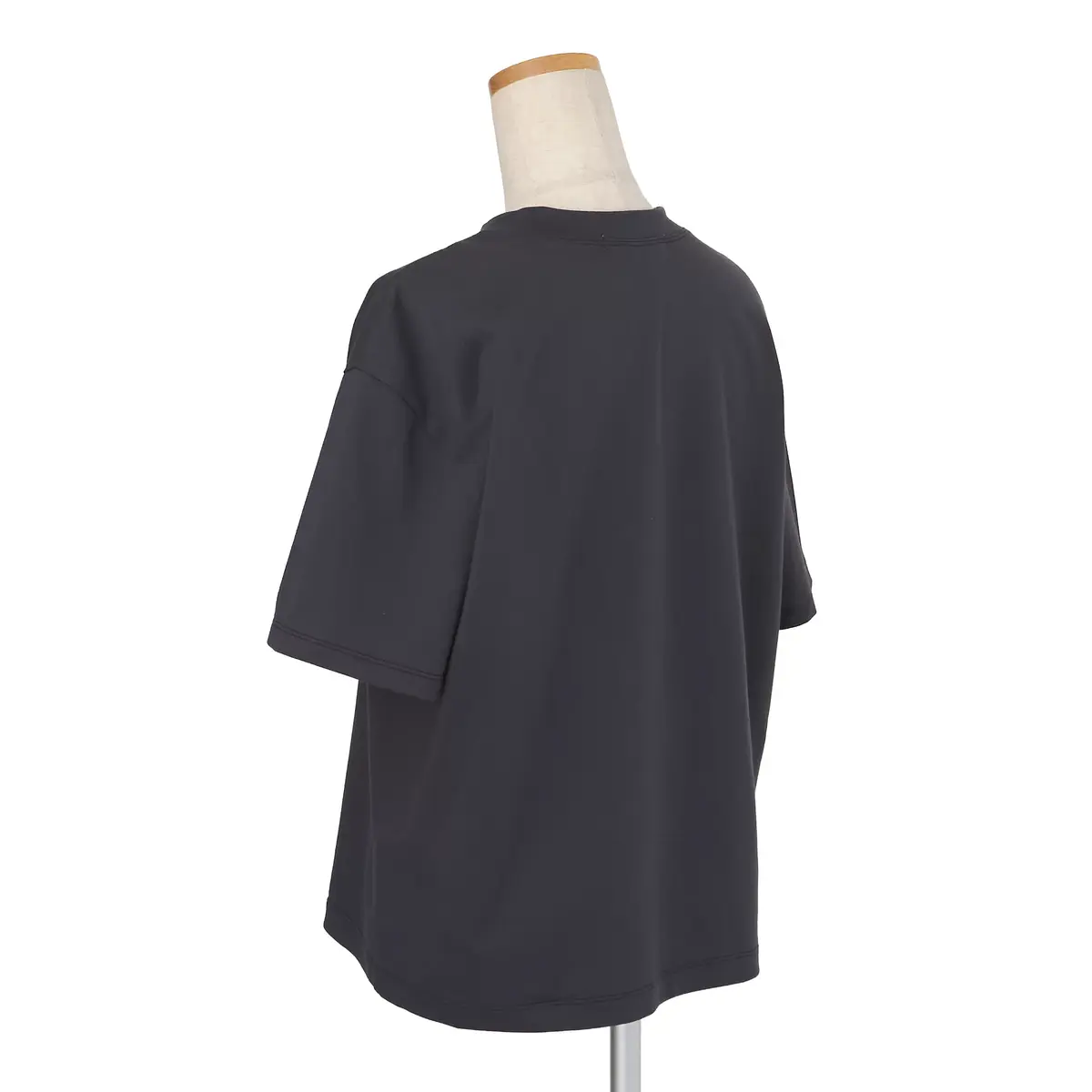 黒色のオーバーサイズTシャツの背面。クルーネックで、ゆったりとしたシルエット。白い縫い目が袖と裾に施されている。マネキンの頭が上部に配置されている。
