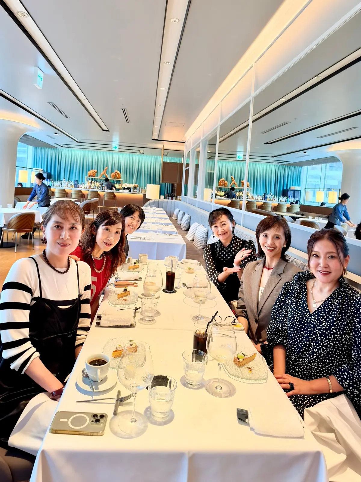 白テーブルを囲み、笑顔の女性6人が写っている。高級レストランのような内装で、窓から景色が見える。テーブルにはグラスや料理が並び、華やかな雰囲気が伝わる。大阪梅田のうめきたエリア、グラングリーンでランチ、お店はブリアンツァ大阪のイタリアンで50代の女子会。