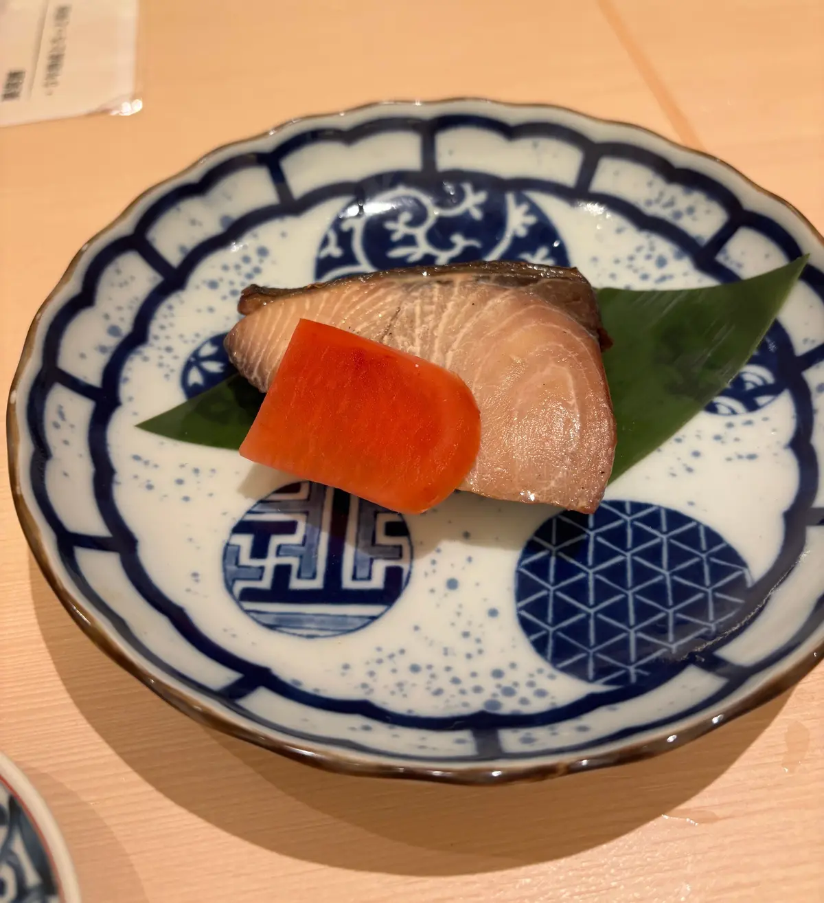青白の和食器に、サーモンにオレンジ色の野菜を添えた料理がのせられている