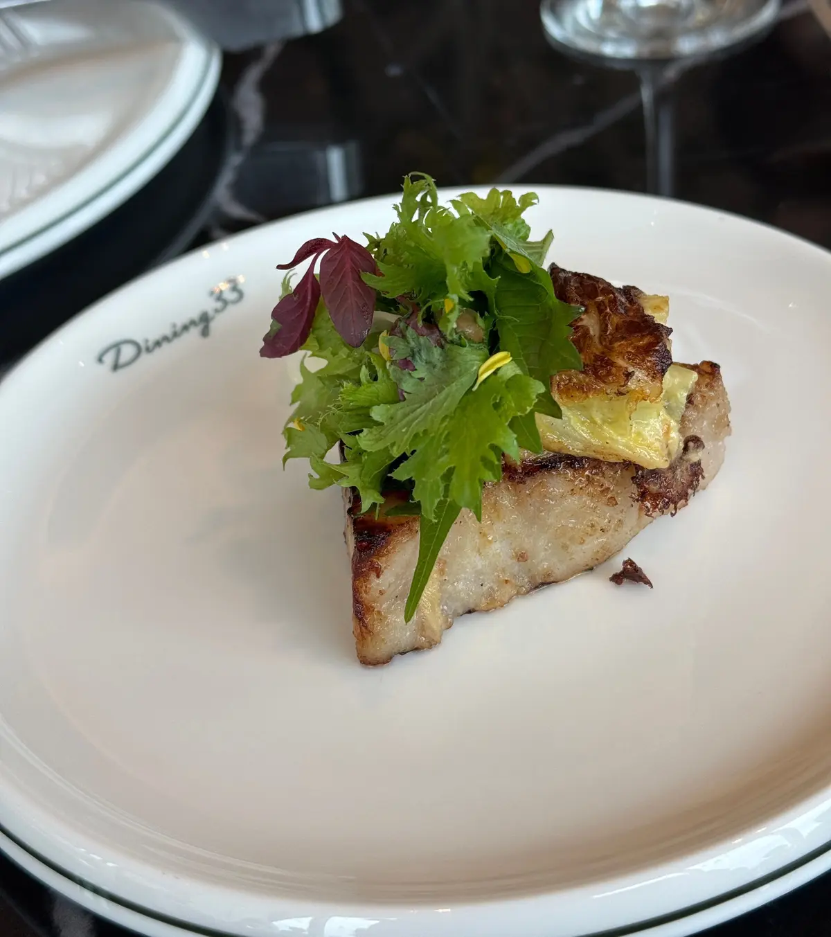 白い皿に盛り付けられた、焼き色のついた三角形の料理。上には緑色の葉野菜が添えられ、Dining 33のロゴが皿に刻印されている。