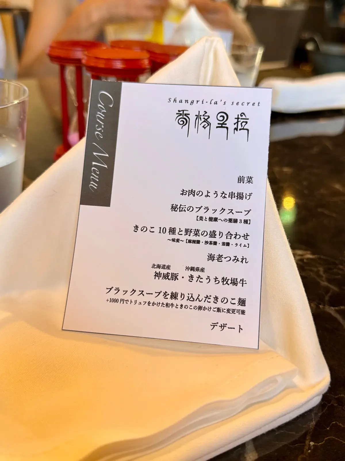 青と白の模様が描かれた陶器製の蓋物と容器が、丸いお皿の上に置かれている。中央の蓋物には金色の取っ手が付いており、背景には木製のテーブルと人物が写っている。