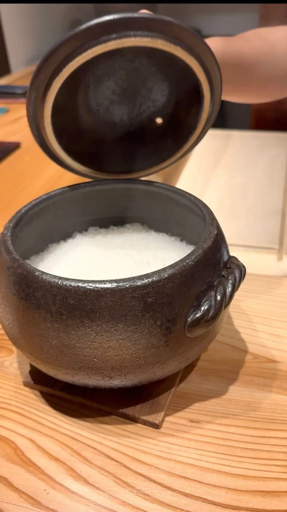 茶色の陶器製の壺と蓋が置かれた木製のテーブル。壺の中には白い粒状のものが詰まっている。蓋は壺から少し離れて傾いている。