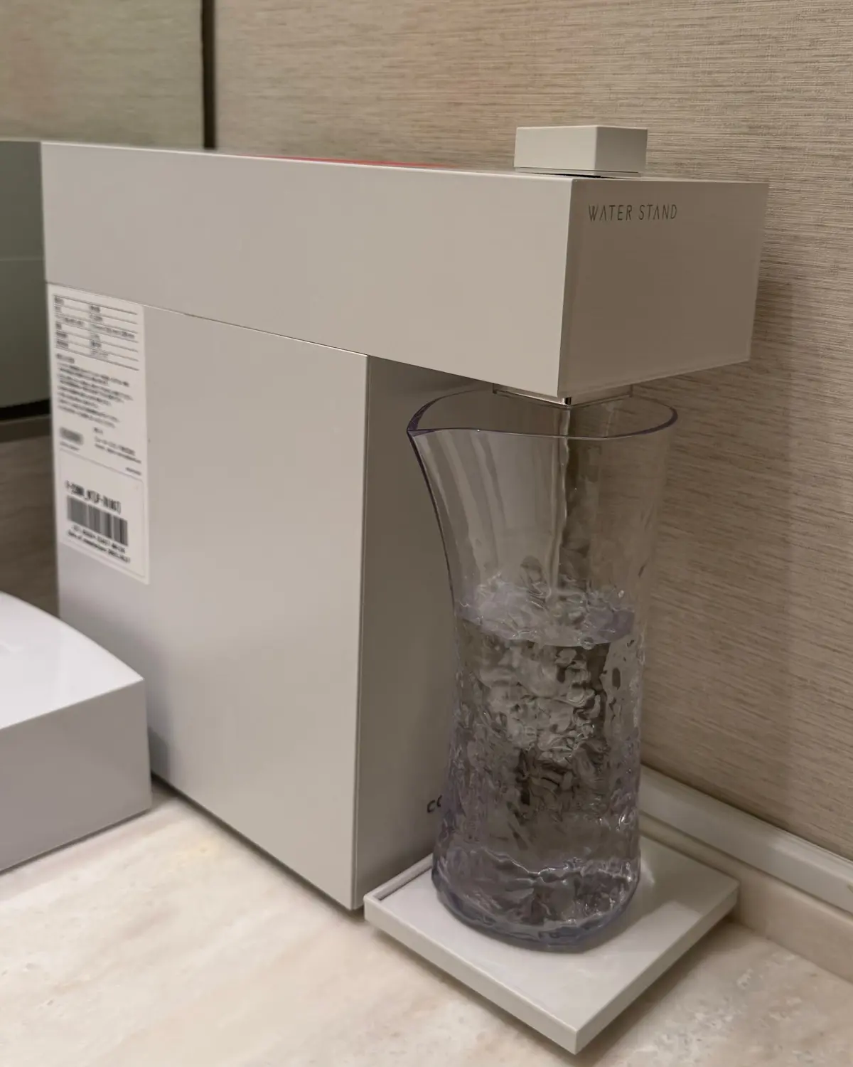白い箱に入った新しい浄水器の横に、氷水を入れた透明なグラスが置かれている。グラスは白い台座に乗せられている。