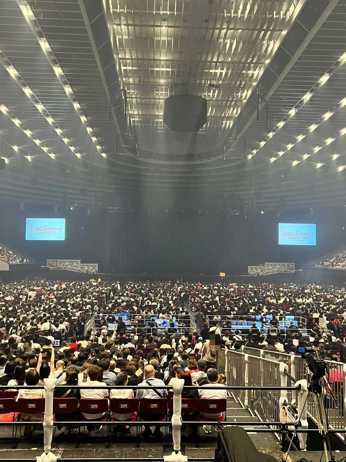 大規模な屋内会場で、数千人の観客が座っている様子。ステージ前方にはSeikoのロゴが掲示され、照明がステージを照らしている。観客席は人で埋め尽くされ、一部の人が手を挙げており、イベントの盛り上がりを伝えている。