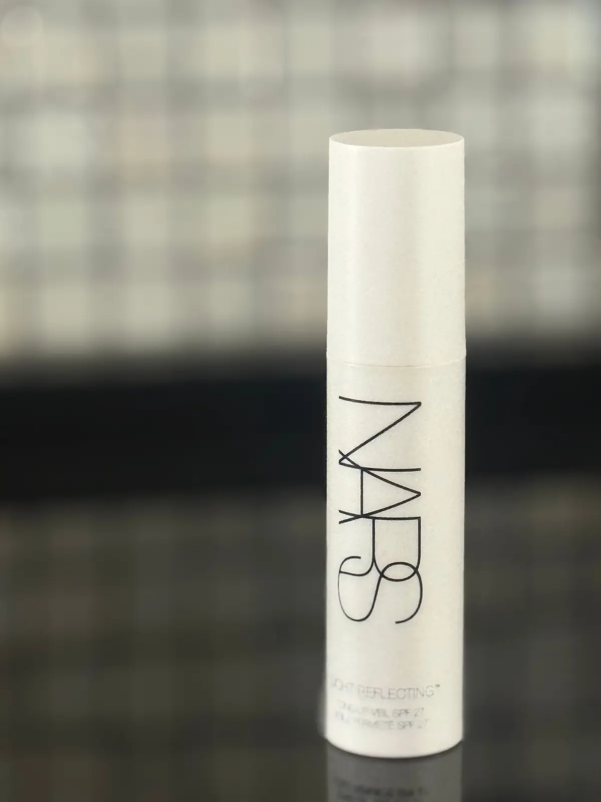 白い円柱形の容器に「NARS」のロゴと「LIGHT REFLECTING」などの文字が印刷され、テーブルの上に置かれている