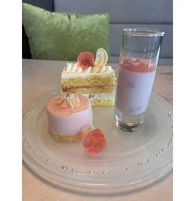 クリアプレートに、ピンクの小さなケーキ、層になった黄色と白のケーキ、グラスにピンクの飲み物と氷が並ぶ。