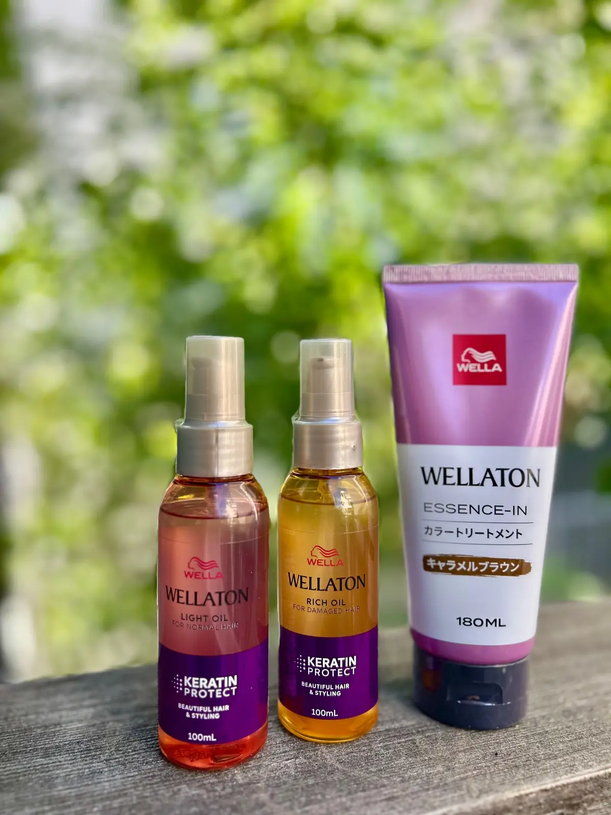 緑の葉の背景に、ウェラ（Wella）のヘアオイル3点が置かれている。左から、ピンクの「ライトオイル」、オレンジの「リッチオイル」、紫色の「エッセンス・イン」のチューブ。いずれも「Keratin Protect」の文字が記載されている。