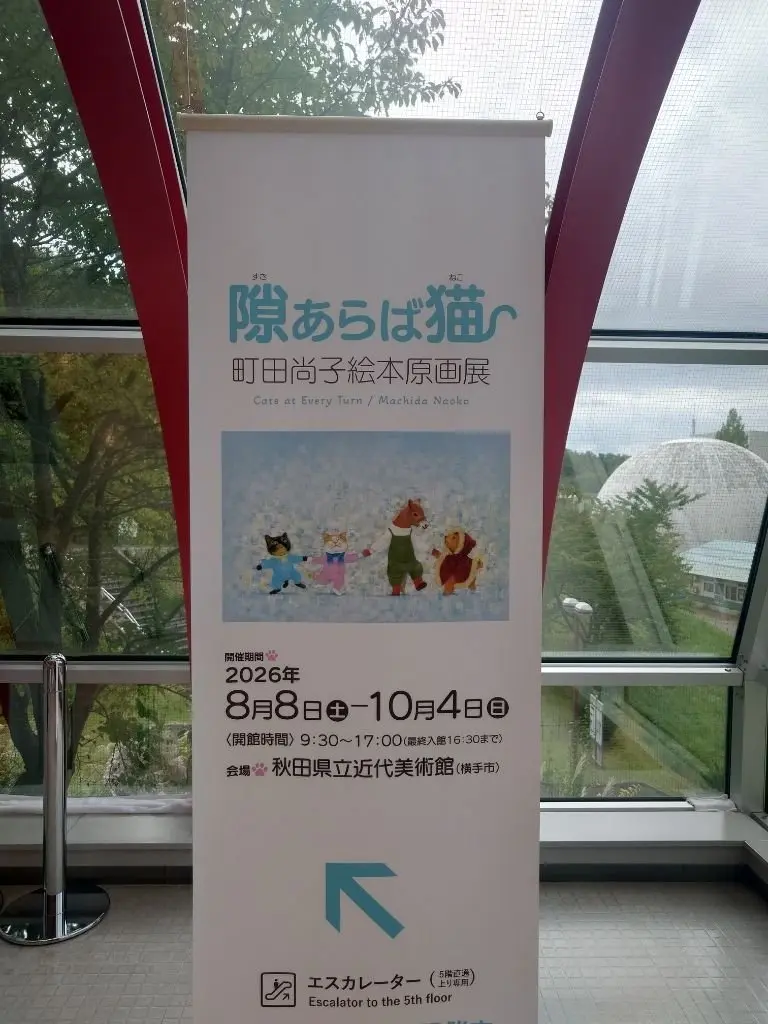 猫のイラストが並んだ展覧会告知ポスター。タイトルは「際はば猫 - 町田治子絵原展」。会期は2026年8月8日から10月4日。会場は秋田県近代美術館。背景には建物が見える。