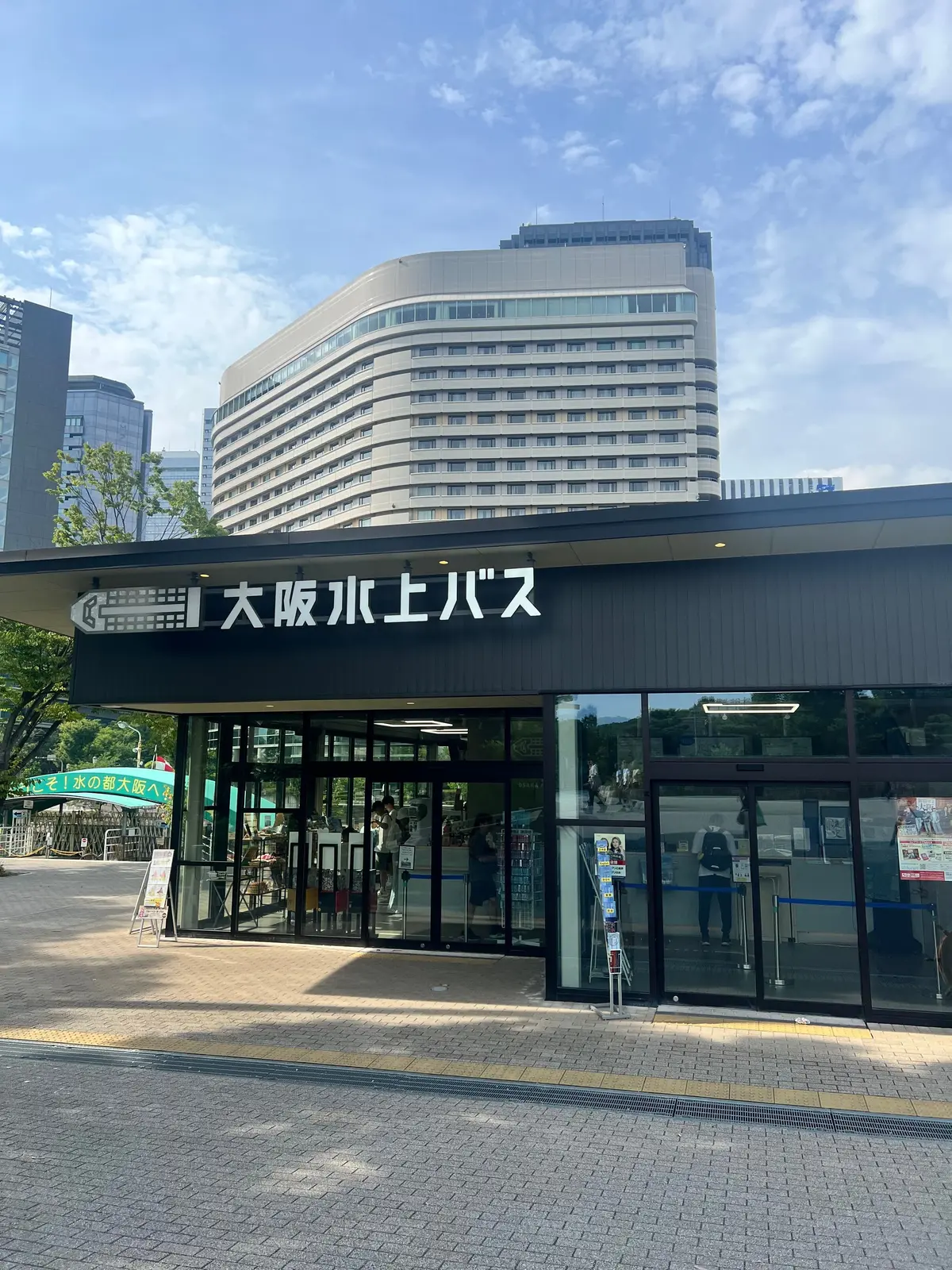 大阪水上バスの乗船口。グレーの建物で、大きな看板に「大阪水上バス」の文字が光る。背景には高層ビル群がそびえ立つ。