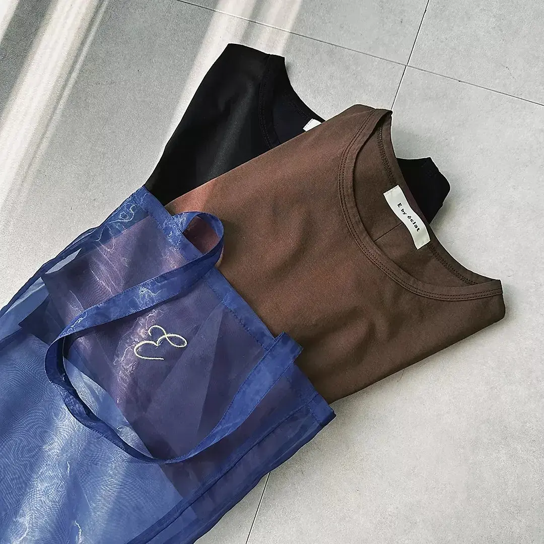 青いメッシュバッグ、茶色のタンクトップ、黒のタンクトップがタイル床に並んでいる
